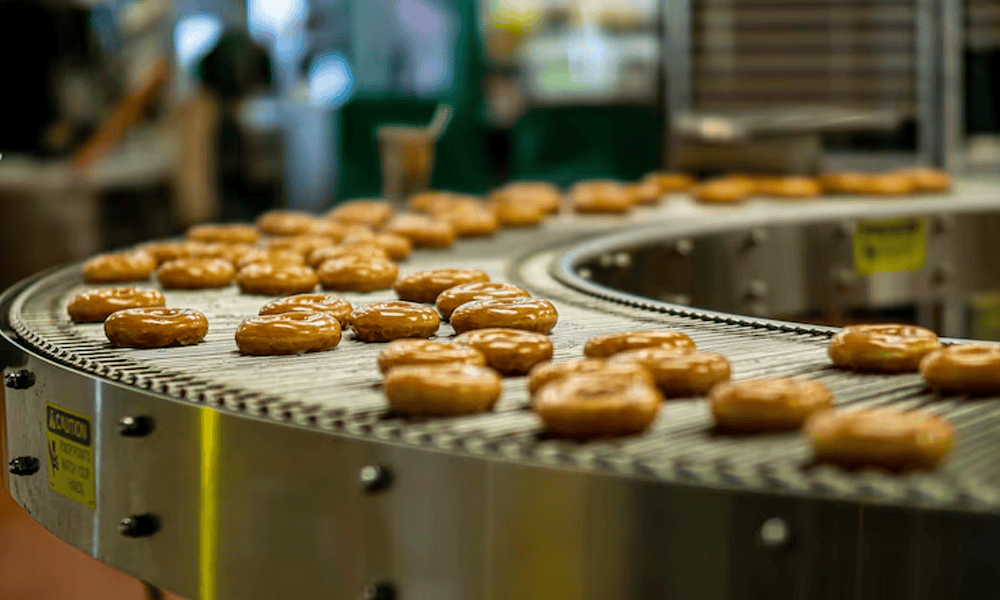 Fresh caramel donuts on a conveyor belt at NK Dairy Equipments manufacturing facility